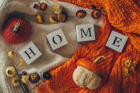 Background with warm sweaters and the inscription HOME. Pile of knitted clothes with autumn leaves, warm background, pumpkins, autumn flowers, knitwear, Autumn concept.の写真素材