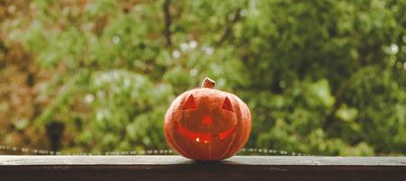 Background Halloween pumpkin on a cozy window sill with a red plaid. Whole pumpkin and sparkler outdoors. Happy Halloween! Autumn is cozy. rain outside.の写真素材