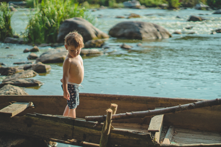 Dreaming boy in old boat at the lake coast. Cute little boy sitting in the old wooden boat on the nature. place for text.の写真素材