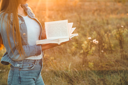 Beautiful girl in autumn field reading a book. The girl sitting on a grass, reading a book. Rest and reading. Outdoor reading.の写真素材