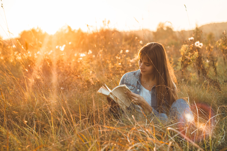 Beautiful girl in autumn field reading a book. The girl sitting on a grass, reading a book. Rest and reading. Outdoor reading.の写真素材