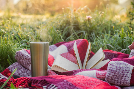 Breakfast with a book in the open air, warm blanket, Steam over a thermo cup. Open book on nature. Book and drinking coffee. Reading at outdoorの写真素材
