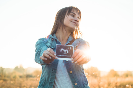 Young Pregnant Woman holding ultrasound photo at Sunset and Embracing her Belly. 4 Month Pregnancy....