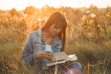 Beautiful girl in autumn field reading a book. The girl sitting on a grass, reading a book. Rest and reading. Outdoor reading.の写真素材