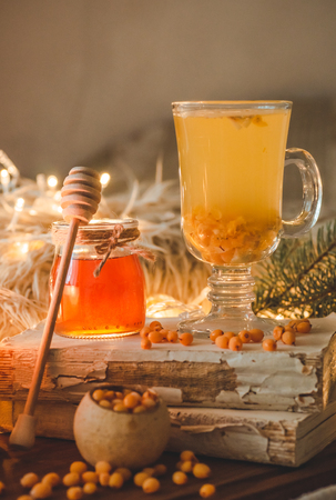 Tea with sea-buckthorn berries and ginger on old books, honey, candle and conifer branches. The atmosphere of comfort at home. Warm cozy home.の写真素材