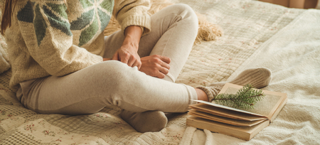 Cozy home. Beautiful girl is reading a book on the bed. Good morning with tea and book. Pretty young girl relaxing. The concept of readingの写真素材