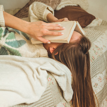 Beautiful young woman sleeping on bed with book covering her face because reading book with preparing exam of college, girl sleepy with tired so that leisure, relax and education concept.の写真素材