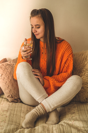 Beautiful Happy Young Woman Drinking Cup Of Coffee Or Tea. In Bed in a bright orange sweater. Closeup Portrait Of Smiling Girl Enjoying Her Drink While Relaxing At Home.の写真素材
