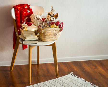 Two winter sweaters laid on a chair with a basket of Christmas decorations, books and led string lights. Winter reading. Winter mood, holiday decoration.の写真素材
