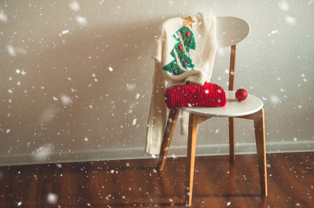 Two winter sweaters laid on a chair with a basket of Christmas decorations and led string lights. Winter mood, holiday decorationの写真素材
