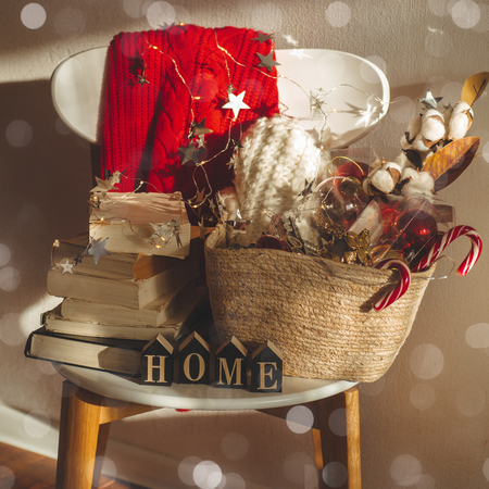 Winter sweater laid on a chair with a basket of Christmas decorations, books and led string lights. Winter mood, holiday decoration with the inscription HOME. Winter reading. House, comfortの写真素材