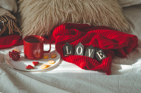 Red cup of tea with kumquat on the plate and two hearts cookies with the word LOVE on a white bed. Valentines day concept. Cozy Homeの写真素材