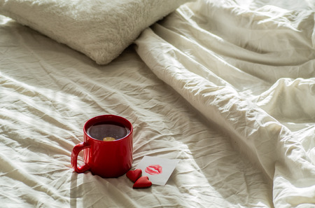 Red cup of tea and two hearts cookies, a note with a kiss on a white bed. Valentines day conceptの写真素材