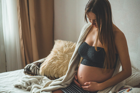 Attractive pregnant woman is sitting in bed and holding her belly. Last months of pregnancyの写真素材