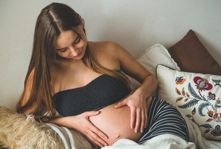 Attractive pregnant woman is sitting in bed and holding her belly. Last months of pregnancyの写真素材