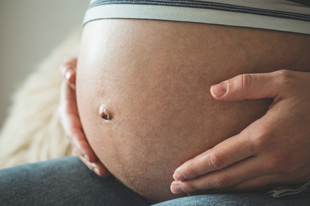 Attractive pregnant woman is sitting in bed and holding her belly. Last months of pregnancyの写真素材