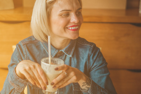 Beautiful girl in a cafe enjoying a cold cocktail. Hipster girl holding summer cocktail. Refreshment drink in sunny dayの写真素材
