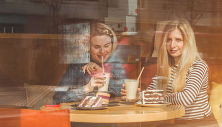 Two happy women sitting in a cafe, drink a cocktail, tell each other funny stories, being in a good mood, laughing happily. Best friendsの写真素材