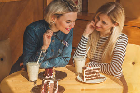 Two happy women sitting in a cafe, drink a cocktail, tell each other funny stories, being in a good mood, laughing happily. Best friendsの写真素材