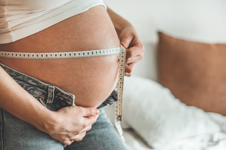 Happy pregnant woman with measuring tape Pregnancy, maternity, preparation and expectation concept. Space for textの写真素材