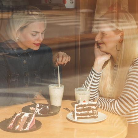 Two happy women sitting in a cafe, drink a cocktail, tell each other funny stories, being in a good mood, laughing happily. Best friendsの写真素材