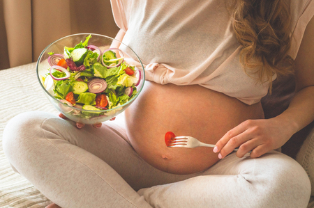 Pregnancy and healthy organic nutrition. Pregnant woman enjoying fresh vegetable salad in bed, free space. Concept of expectation and health.の写真素材
