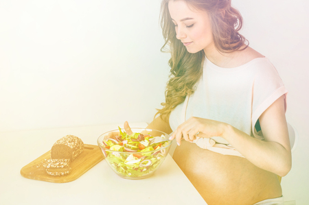 Pregnancy and healthy organic nutrition. Pregnant woman enjoying fresh vegetable salad in bed, free space. Concept of expectation and health.の写真素材