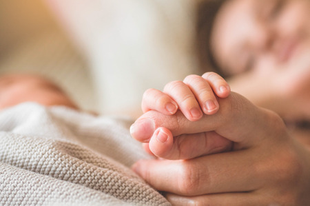 Female hand holding her newborn baby hand. Mom with her child. Maternity, family, birth concept. Copy space for your text.の写真素材