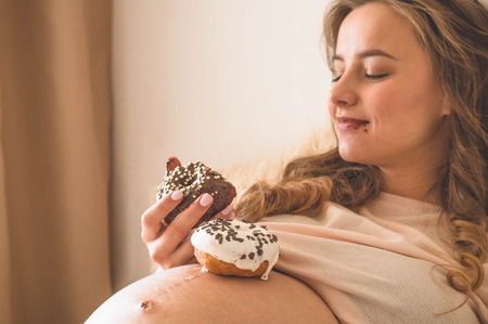 Pregnancy and nutrition. Pregnant woman enjoying donuts and tea in bed, free space. Concept of...