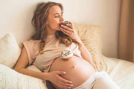 Pregnancy and nutrition. Pregnant woman enjoying donuts and tea in bed, free space. Concept of expectation and health.の写真素材