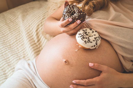 Pregnancy and nutrition. Pregnant woman enjoying donuts and tea in bed, free space. Concept of expectation and health.の写真素材