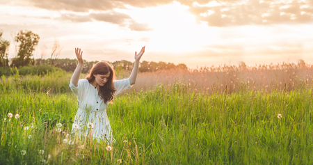 Girl closed her eyes, praying in a field during beautiful sunset. Hands folded in prayer concept for faith, spirituality and religion. Peace, hope, dreams conceptの写真素材