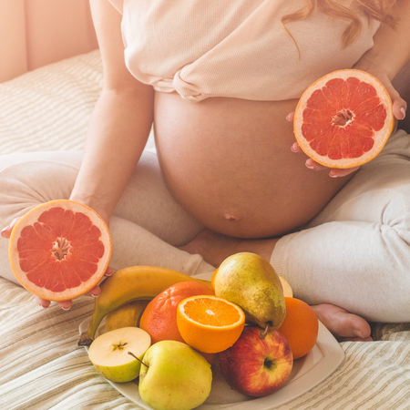 Pregnancy and healthy organic nutrition. Pregnancy and grapefruit. Pregnant woman enjoying fresh fruits in bed, free space. Concept of expectation and healthの写真素材