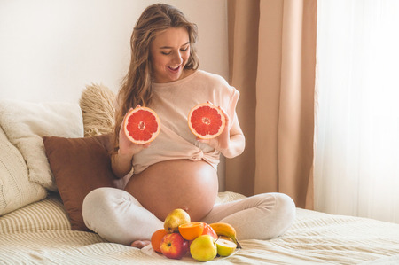 Pregnancy and healthy organic nutrition. Pregnancy and grapefruit. Pregnant woman enjoying fresh fruits in bed, free space. Concept of expectation and healthの写真素材