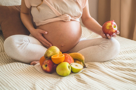 Pregnancy and healthy organic nutrition. Pregnancy and grapefruit. Pregnant woman enjoying fresh fruits in bed, free space. Concept of expectation and healthの写真素材