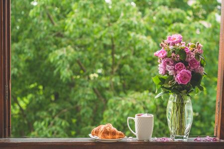 Book, croissant, cup of tea and roses on a wooden window. Read books. Romantic concept. Vintage styleの写真素材