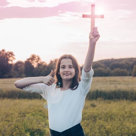 Teenager Girl holding a the cross in hand during beautiful sunset. Hands folded in prayer concept...
