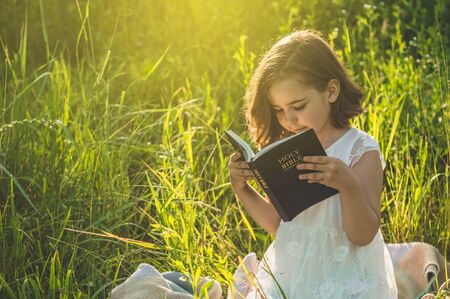 Christian girl holds bible in her hands. Reading the Holy Bible in a field during beautiful sunset. Concept for faith, spirituality and religion. Peace, hopeの写真素材