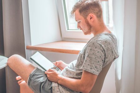 Technology, home - lifestyle concept close up of man working with the tablet computer and sitting on chair at home.の写真素材