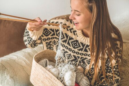 Beautiful girl knits a warm sweater on the bed. Knitting as a hobby. Accessories for knitting.の写真素材