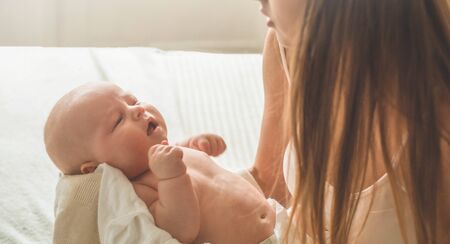 Home portrait of a newborn baby with mother on the bed. Mom holding and kissing her child. Concept breast feeding.の写真素材