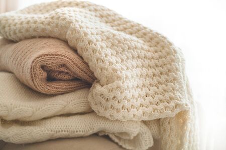 A stack of knitted sweaters in the interior of the living room. The concept of autumn winter comfort