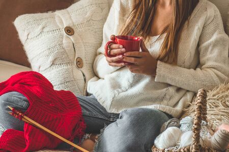Beautiful girl knits a warm sweater with a hot cup of tea on the bed. Knitting as a hobby. Accessories for knitting.の写真素材