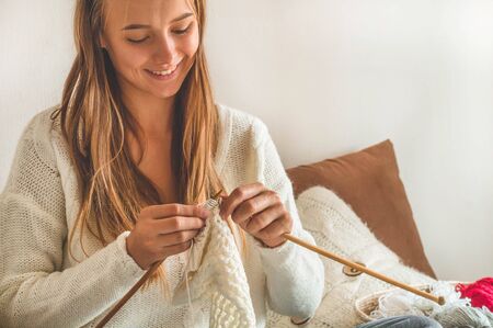 Beautiful girl knits a warm sweater on the bed. Knitting as a hobby. Accessories for knitting.の写真素材