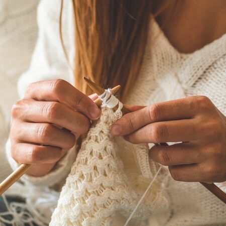 Beautiful girl knits a warm sweater on the bed. Knitting as a hobby. Accessories for knitting.の写真素材