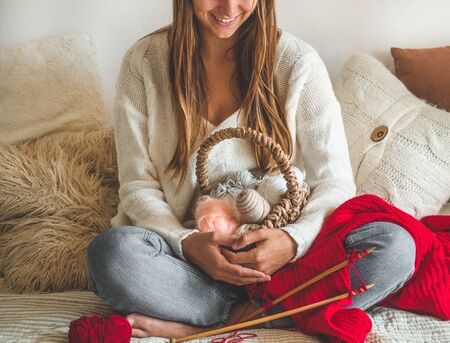 Beautiful girl knits a warm sweater on the bed. Knitting as a hobby. Accessories for knitting.の写真素材