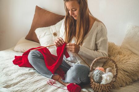 Beautiful girl knits a warm sweater on the bed. Knitting as a hobby. Accessories for knitting.の写真素材