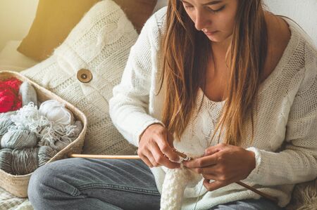 Beautiful girl knits a warm sweater on the bed. Knitting as a hobby. Accessories for knitting.の写真素材