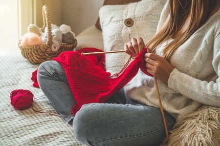 Beautiful girl knits a warm sweater on the bed. Knitting as a hobby. Accessories for knitting.の写真素材
