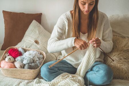 Beautiful girl knits a warm sweater on the bed. Knitting as a hobby. Accessories for knitting.の写真素材